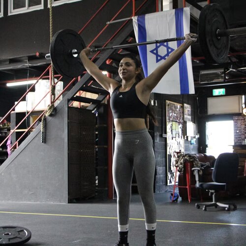 מתאמנת מחזיקה מוט מעל הראש באימון CrossFit